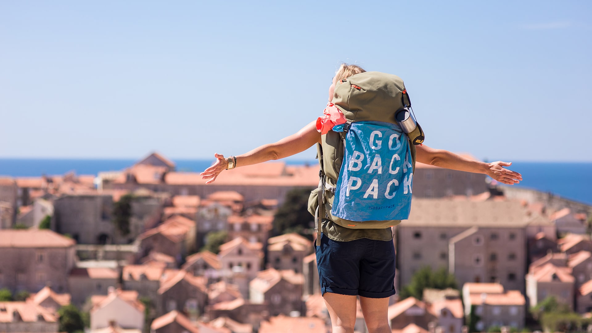 Junge Frau steht mit ausgebreiteten Armen vor einer Stadt für die Jack Wolfskin Kampagne #GOBACKPACK