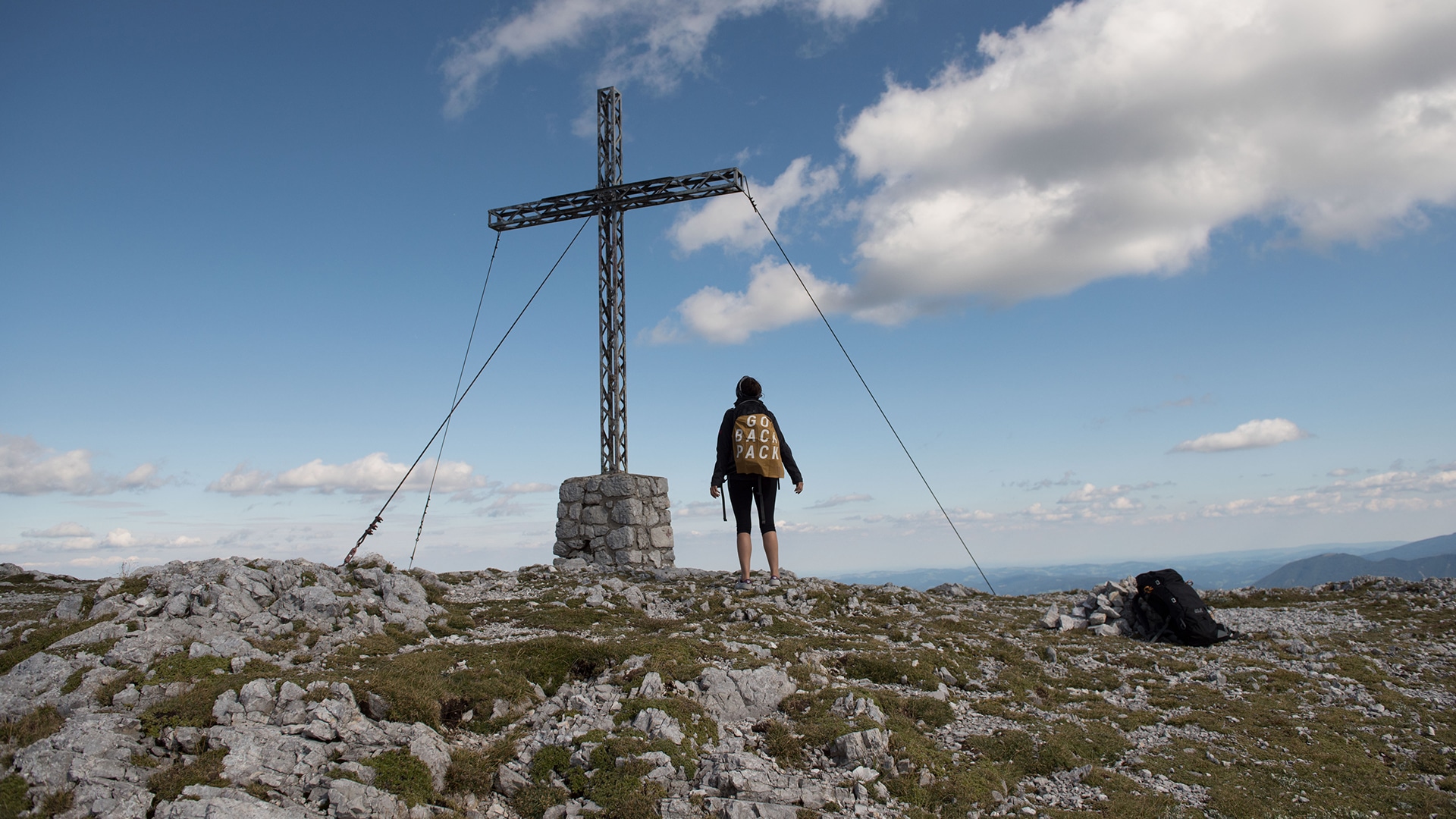 Junge Frau steht auf einem Berggipfel für die Jack Wolfskin Kampagne #GOBACKPACK