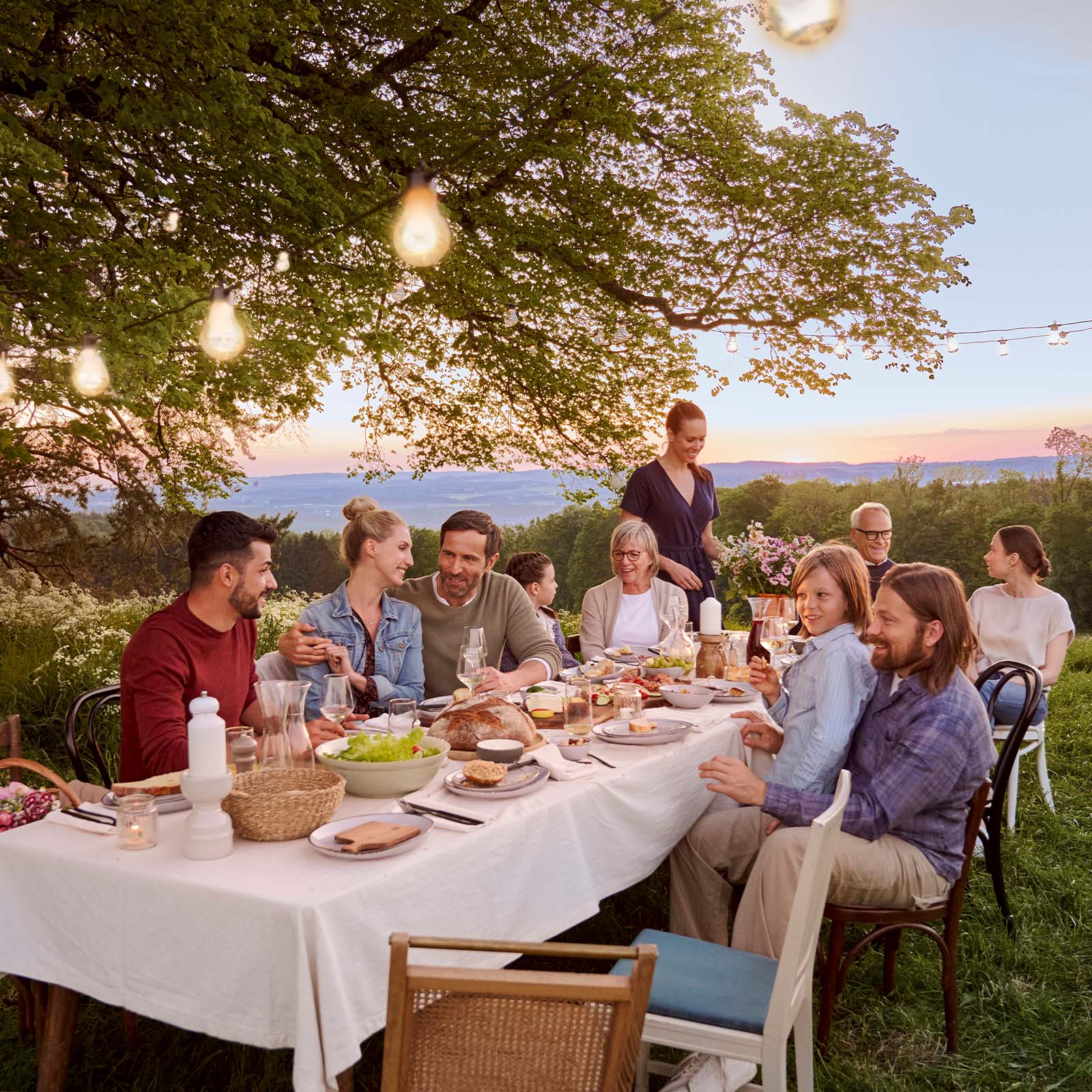 Familie sitzt unter einem Baum am Tisch und reden