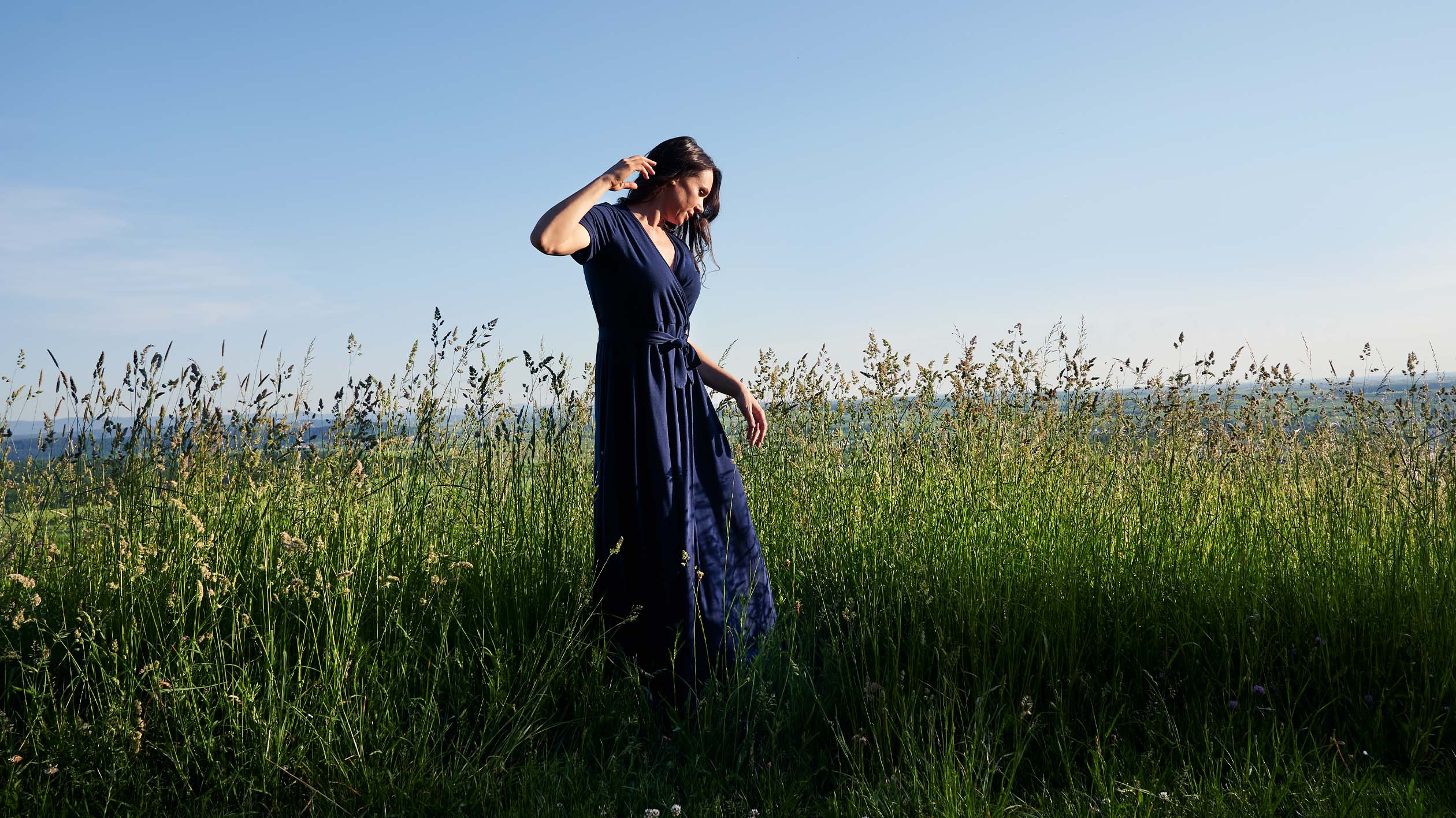 Frau in blauem Kleid steht in hohem Gras