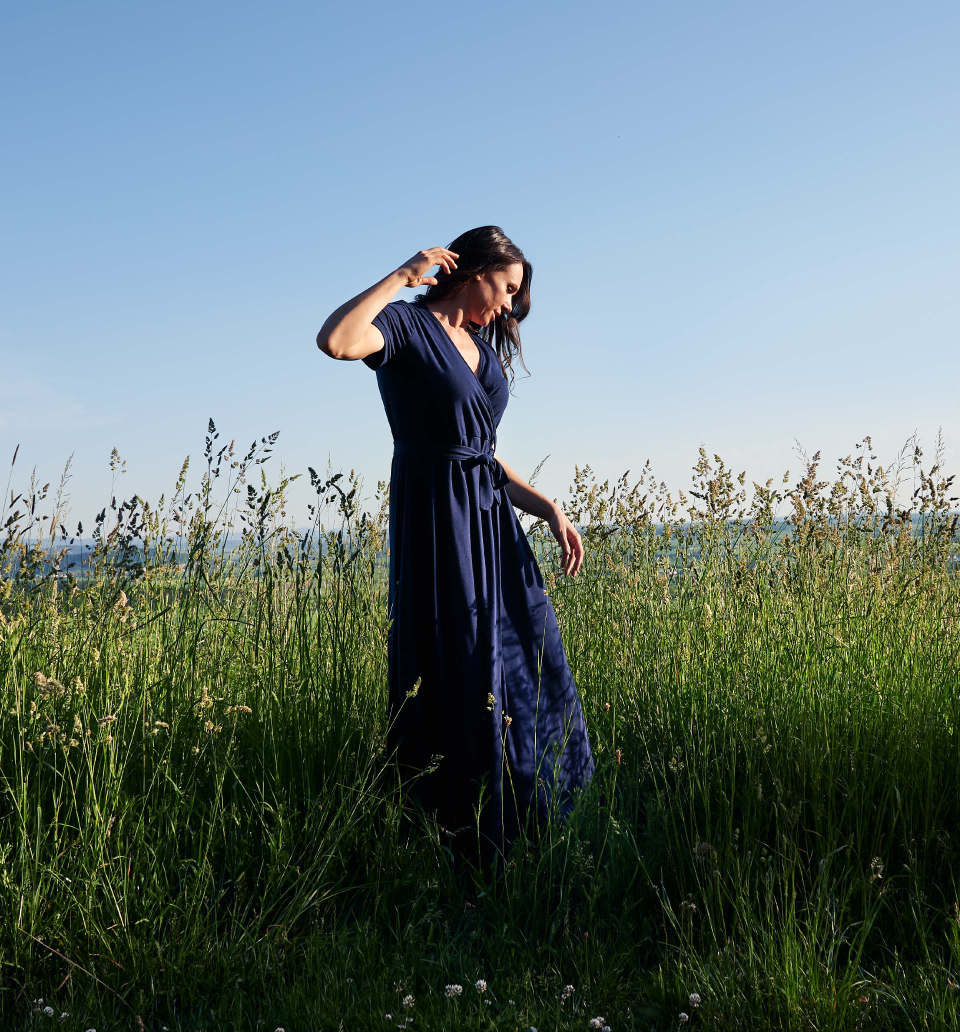 Frau in blauem Kleid steht in hohem Gras